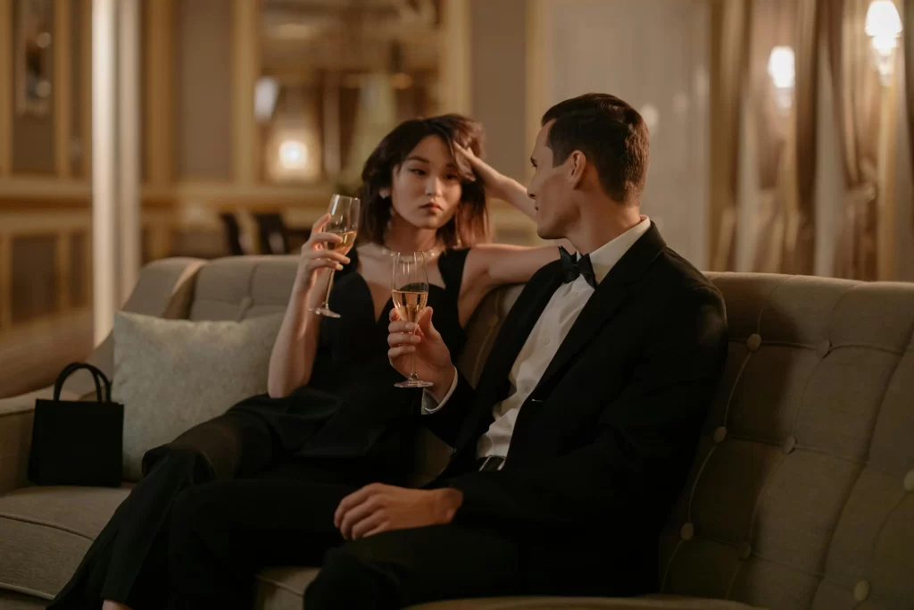 Well dressed white man and an asian woman on a couch drinking champagne
