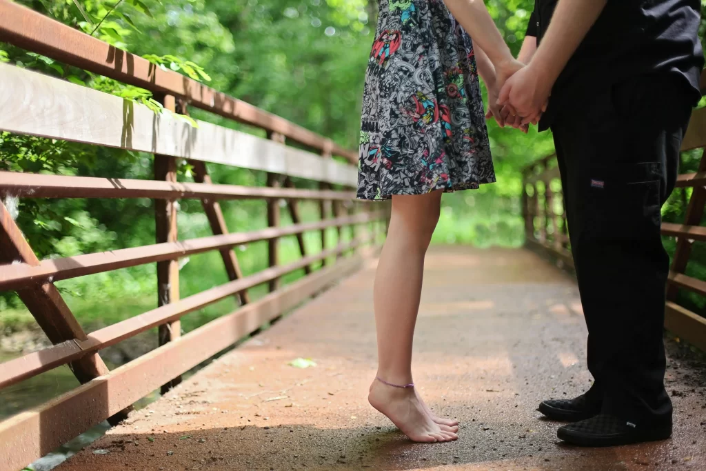 Woman on her toes kissing a man in a park on a bridge