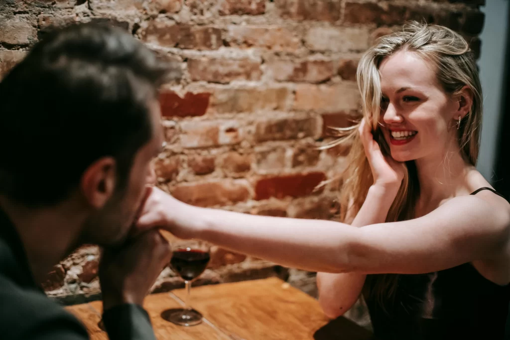 Man and woman on a date in a bar at a wooden table. She is laughing and touching his hand.