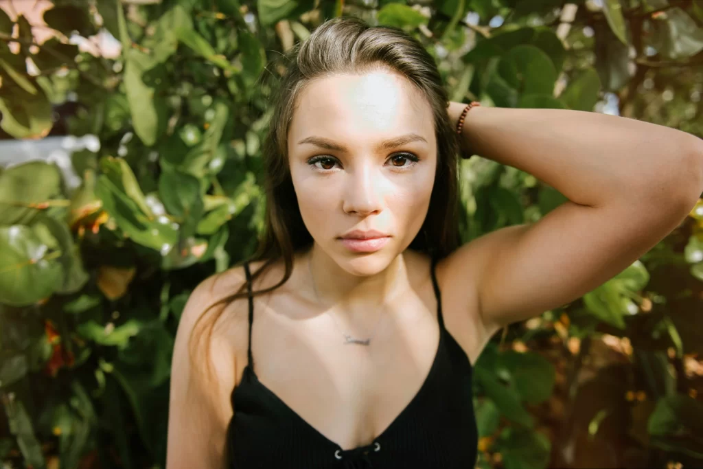 Nervous looking girl in black tank top with green leaves behind her