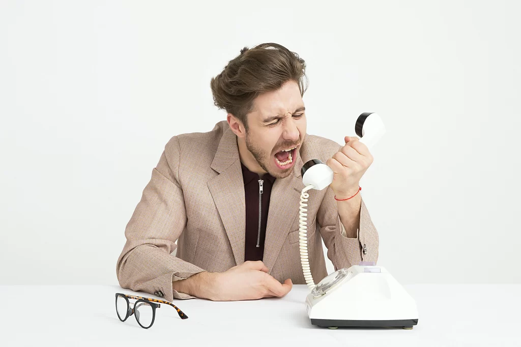 A man in a white room yelling angrily into a telephone