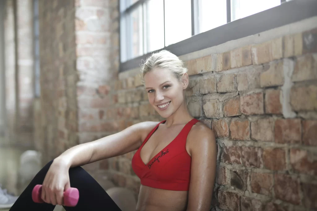 Blonde girl sitting against a brick wall in a red tank top 