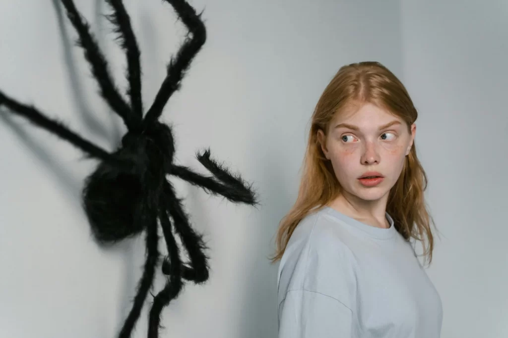 A giant fake spider on the wall beside a young woman