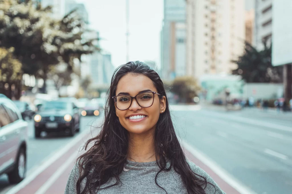 Brown skinned woman with glasses smiling on a city street