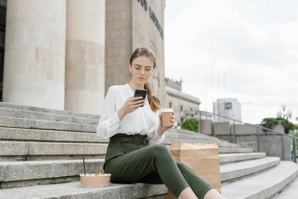 A professional woman sitting on city steps looking at her phone