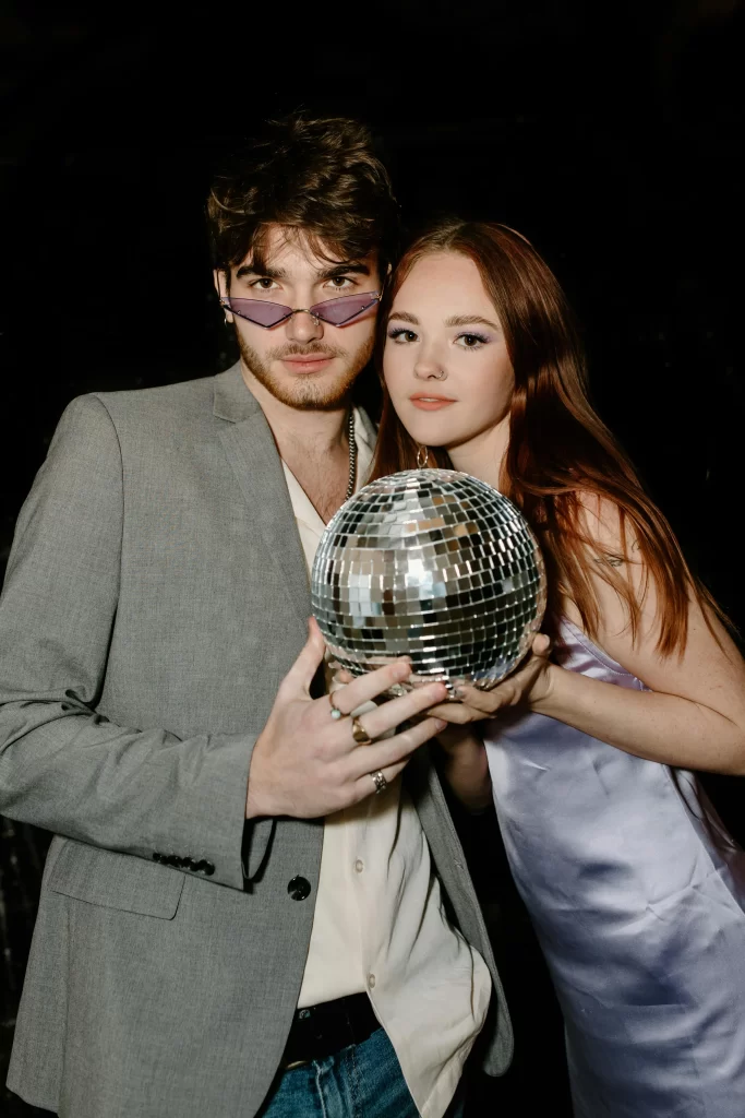 Man in a grey blazer with a girl in a silver dress holding a disco ball